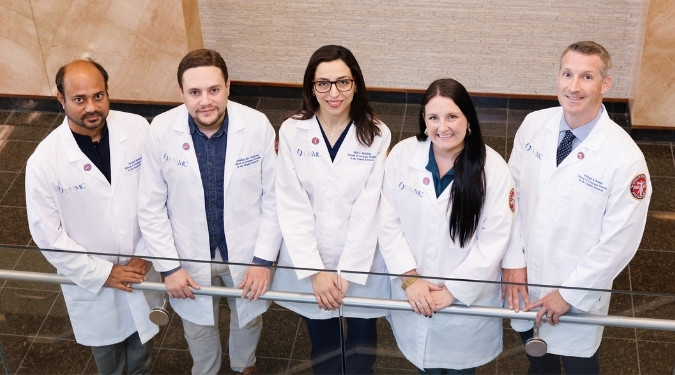 A group of clinical anatomy graduate students in their white lab coats smile.